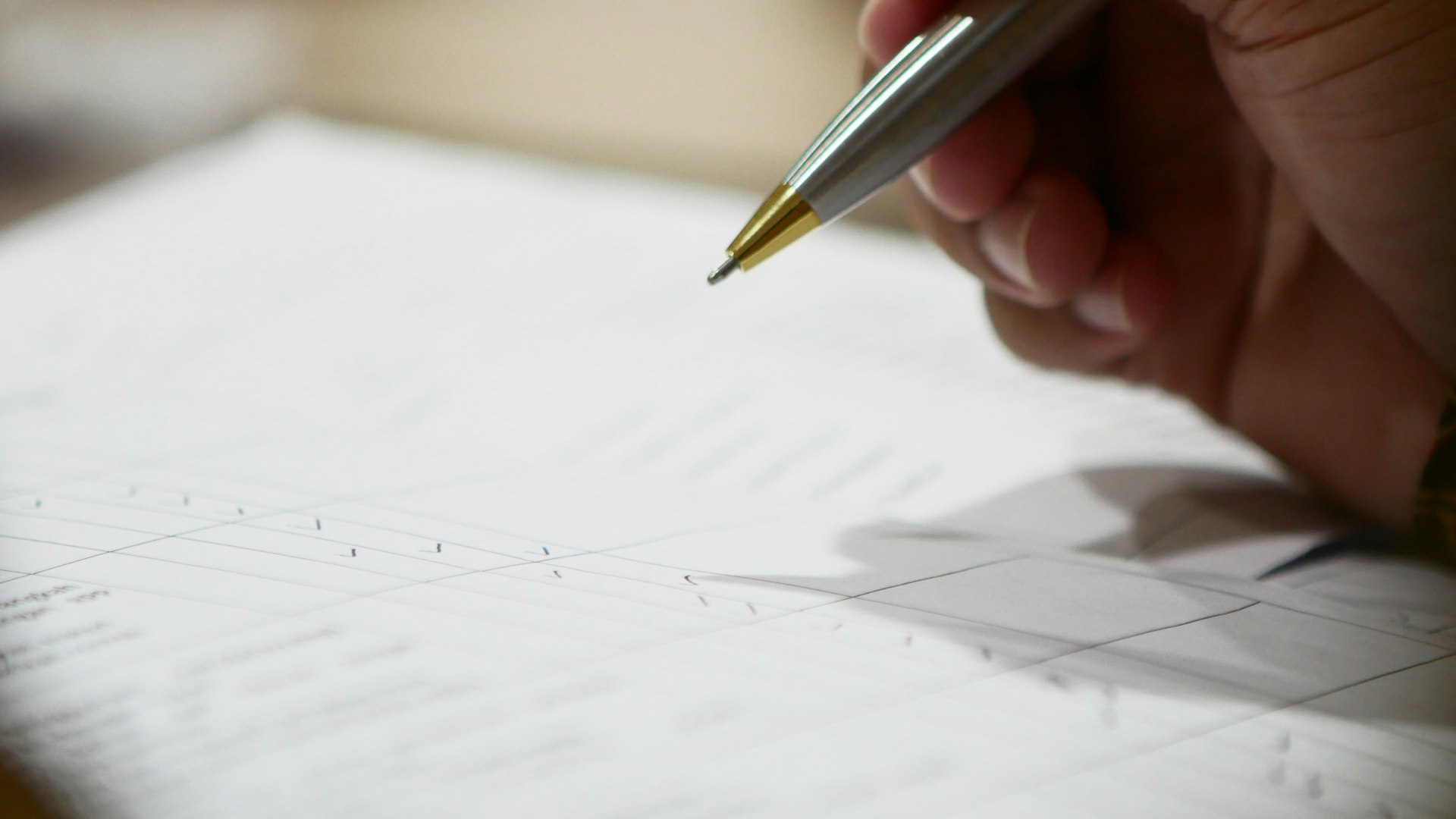 A hand holding a pen over a printed sheet with a table